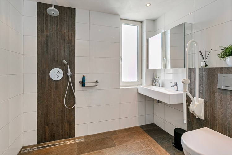 De ruime badkamer is voorzien van een anti-slip tegelvloer (indirecte vloerverwarming), volledig betegelde wanden en een stucwerk plafond. Met een inloopdouche met een regendouche en een in de wand geïntegreerde thermostaatkraan,  een wastafel met een spiegelkast en een wandcloset.