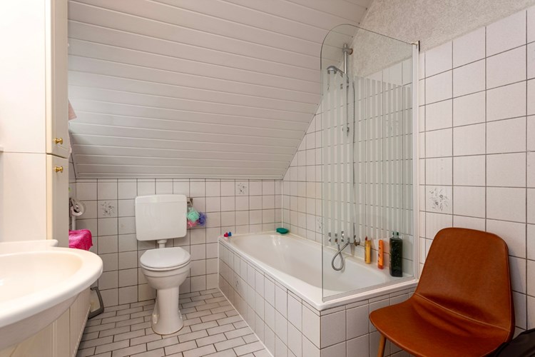 Badkamer met een lichte tegelvloer, volledig licht betegelde wanden en een kunststof schroten plafondafwerking. Met een 2e toilet en een ligbad met thermostaatkraan, spatscherm en douchemogelijkheid. 