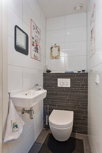 Volledig betegeld toilet met een antraciet vloer en een stucwerk plafond. Met een wandcloset met een opzetplateau, een fonteintje en mechanische ventilatie.