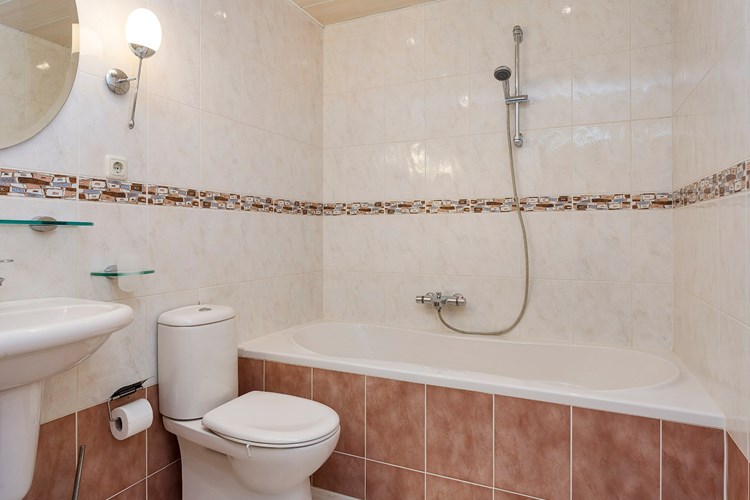 Badkamer (2e) met een lichte tegelvloer, volledig betegelde wanden en een kunststof panelen plafond met inbouwspots. Met een toilet en een kunststof ligbad met thermostaatkraan en douchegarnituur. 