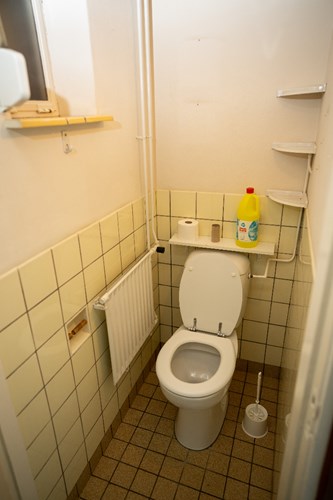 Gedeeltelijk betegeld toilet met een duoblok en een raampje. 
