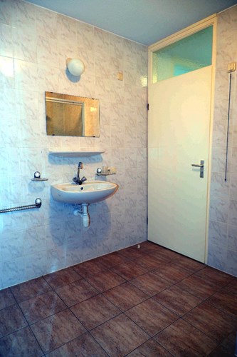 Badkamer met een tegelvloer, volledig licht betegelde wanden en een spuitwerk plafond. Met een wastafel met spiegel.